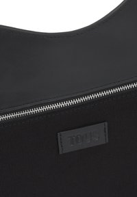 Borsa tote in tessuto nero con finitura liscia, dotata di una cerniera argentata e logo "TOUS" impresso su una targhetta in pelle. Design semplice e materiale strutturato.