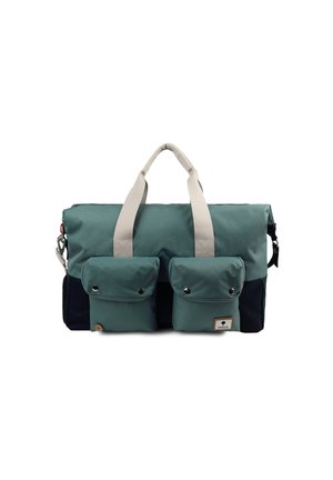 Rectangular duffel bag in teal and navy, featuring two front pockets with snaps, beige handles, and a fabric label tag. Made of durable material.