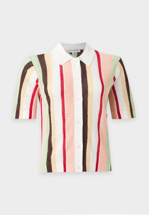 Femme portant une chemise à manches courtes boutonnée avec des rayures verticales colorées et un pantalon large rayé verticalement rose et noir.