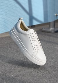 Sneaker in pelle bianca con design a basso profilo, punta rotonda, lacci piatti e colletto imbottito. Interno chiaro e suola testurizzata.