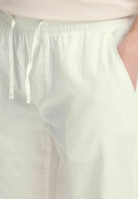Lichtbeige broek met een elastische tailleband, trekkoorddetail, zijzakken en een gestructureerde stof die lijkt op linnen.
