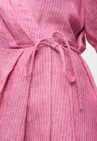 Κοντινή λήψη ενός ροζ ριγωτού υφασμάτινου φόρεματος τύπου wrap, δεμένου με φιόγκο στη μέση.