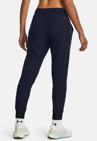 Navy athletic pants with an elastic waistband, tapered cuffs, and side pockets. Made of lightweight fabric with a smooth texture.