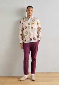 Short-sleeve, light pink shirt with colorful floral and graphic patterns, paired with burgundy pants and beige loafers over white socks.