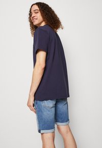 T-shirt in cotone blu navy con maniche corte, indossato con pantaloni shorts in denim azzurro arrotolati, con un effetto sbiadito e dettagli strappati.