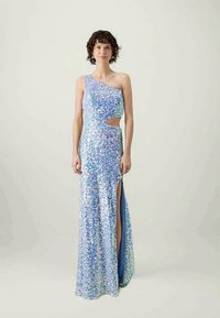 Sieviete, tērpusies spīdīgā gaiši z blue viendaļīgā kleitā ar sānu izgriezumu un augstu šķēlumu, stāv uz vienkārša fona.