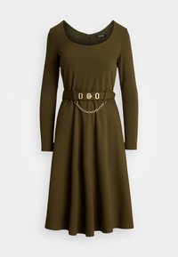 Olivově zelené šaty s dlouhým rukávem, kulatým výstřihem, přiléhavým pasem a páskem se zlatým řetízkem a sponou.