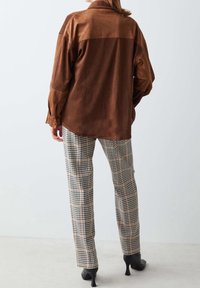 Brązowa koszula z zamszu z jaśniejszym panelem na górze, w połączeniu z czarno-białymi spodniami w kratę. Strój ma dopasowane nogawki i czarne szpilki.