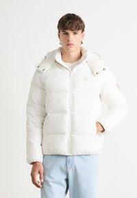 Vit pufferjacka med en figursydd design, dragkedjestängning och huva. Har en quiltad yta och logotyp accent på bröstet.
