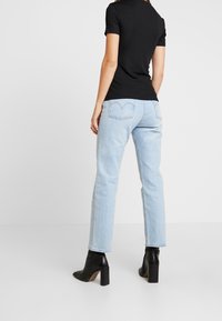 Vaqueros rectos azul claro con bolsillos traseros, combinados con una camiseta negra ajustada. La modelo lleva botas de tobillo negras con tacón.