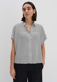 Blusa a maniche corte a righe bianche e nere con chiusura a bottoni e colletto. Tessuto morbido con vestibilità ampia e spacchi laterali all'orlo.