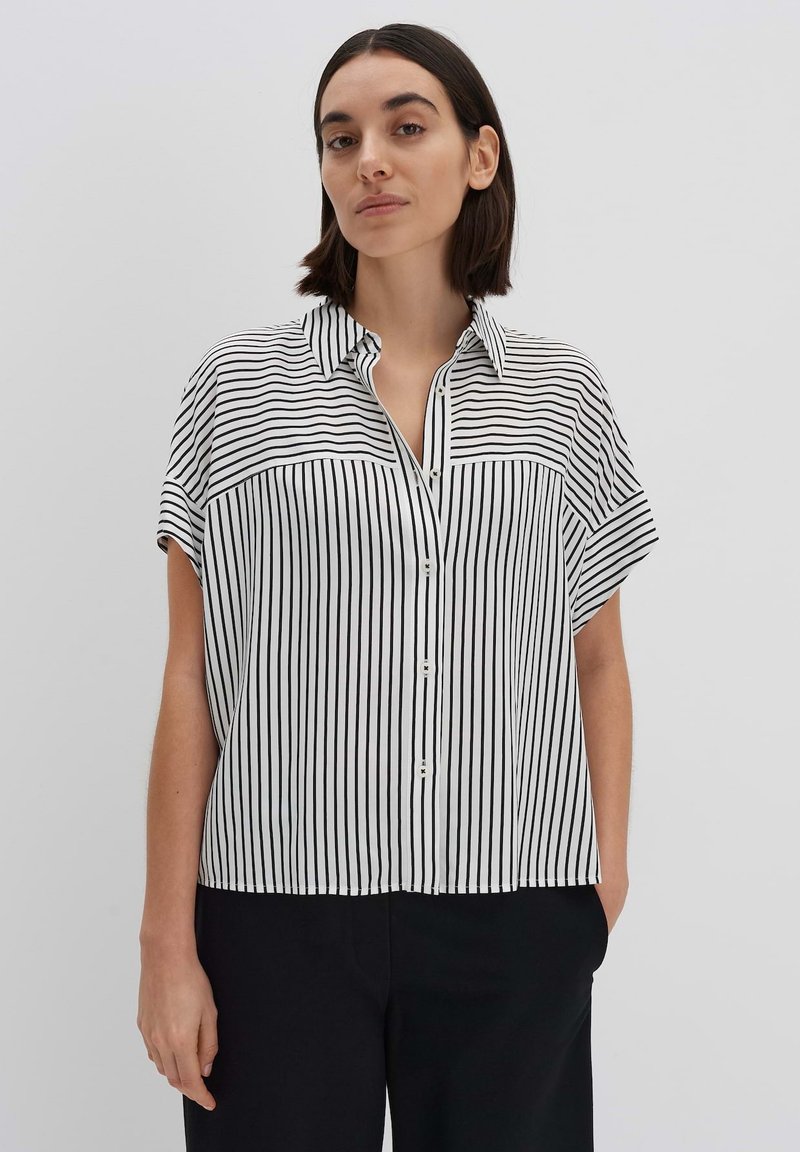 Blusa a maniche corte a righe bianche e nere con chiusura a bottoni e colletto. Tessuto morbido con vestibilità ampia e spacchi laterali all'orlo.