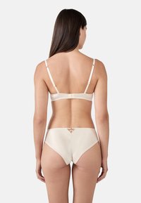 Set di lingerie beige morbido caratterizzato da una finitura satinata liscia. Il reggiseno ha spalline regolabili e una chiusura a gancio; le mutandine presentano un raffinato taglio sul retro.