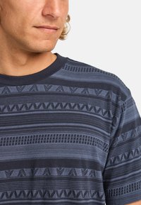 Short-sleeve navy blue t-shirt featuring textured stripes and geometric patterns in varying shades of blue and black.