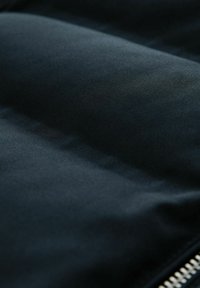 Tissu rembourré noir avec une texture lisse, présentant un léger éclat et une fermeture éclair argentée le long du bord. Aucun motif ou accent notable visible.