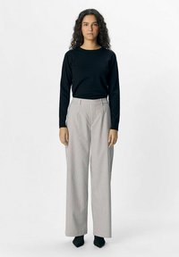 Schwarzes Langarmoberteil kombiniert mit weiten gestreiften Hosen in Grau und Weiß, mit hoher Taille und glatter Textur. Schwarze spitz zulaufende Schuhe.