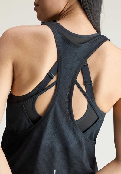 Close-up of a woman’s upper back wearing a black mesh racerback tank top layered over a strappy black sports bra.