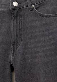 Gros plan sur un jean en denim noir montrant la poche avant, la fermeture à bouton, la passante de ceinture et les détails de couture visibles.