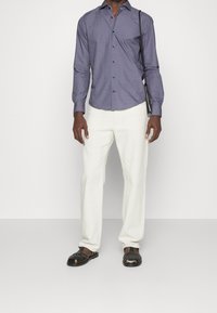 Heren overhemd met lange mouwen in donkerpaars met een klein geometrisch patroon, gecombineerd met witte linnen broek en zwarte geweven sandalen.