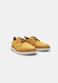 Scarpe in pelle gialla con superficie texture, lacci marroni e suola bianca a contrasto. Presentano un bordo cucito e un tassello sul tallone.