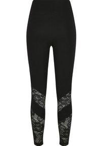 Leggings noirs avec une large ceinture, présentant des inserts en dentelle en motif chevron sur les côtés inférieurs. Texture de tissu lisse et extensible.