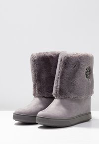 Bottes chevilles grises avec un revers en fausse fourrure, présentant une finition en daim lisse, un bout arrondi et une semelle en caoutchouc texturée avec un accent logo.