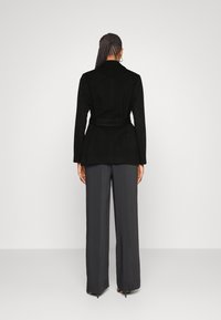 Blazer negro a medida con cintura ceñida, combinado con pantalones anchos de pierna oscura. Tejido liso, diseño estructurado y sin patrones visibles.