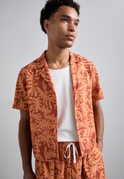 Short-sleeve shirt in orange cotton with a tan leaf pattern, paired with matching shorts. Features a relaxed fit and button front.