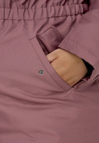 Purple waterproof jacket with a textured finish, featuring an elastic waistband and side pocket with snap button detail.