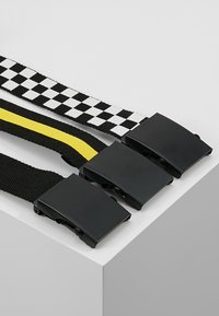 Drei geflochtene Gürtel, horizontal ausgestellt: einer mit einem schwarz-weißen karierten Muster, einer mit einem einfarbigen schwarzen Grund und gelber Streifen, und ein anderer in Schwarz.