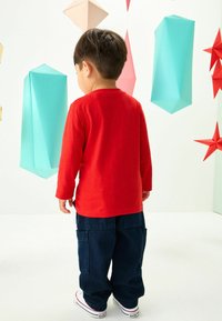 Chemise rouge à manches longues et pantalon cargo bleu marine foncé. La chemise a un col rond, tandis que le pantalon possède des poches latérales.