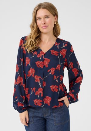 Blouse marine avec motif floral rouge, décolleté en V, et détail de boutons à l'avant. Manches longues, froncées avec poignets. Tissu léger et lisse.