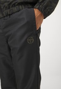 Pantaloni sportivi neri realizzati in tessuto leggero, con una texture sottile, tasche laterali e un logo a contrasto in oliva.