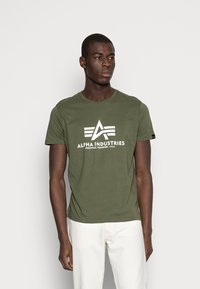 Olivgrünes Baumwoll-T-Shirt mit Rundhalsausschnitt, das einen weißen Logo-Druck und stilisierten Text zeigt. Kurze Ärmel und gerade Säume.