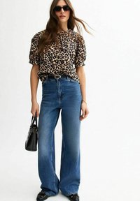 Blouse met luipaardprint en korte mouwen, hoge taille met wijde blauwe jeans en zwarte handtas. Glad materiaal en een losse fit. Zwarte zonnebril.