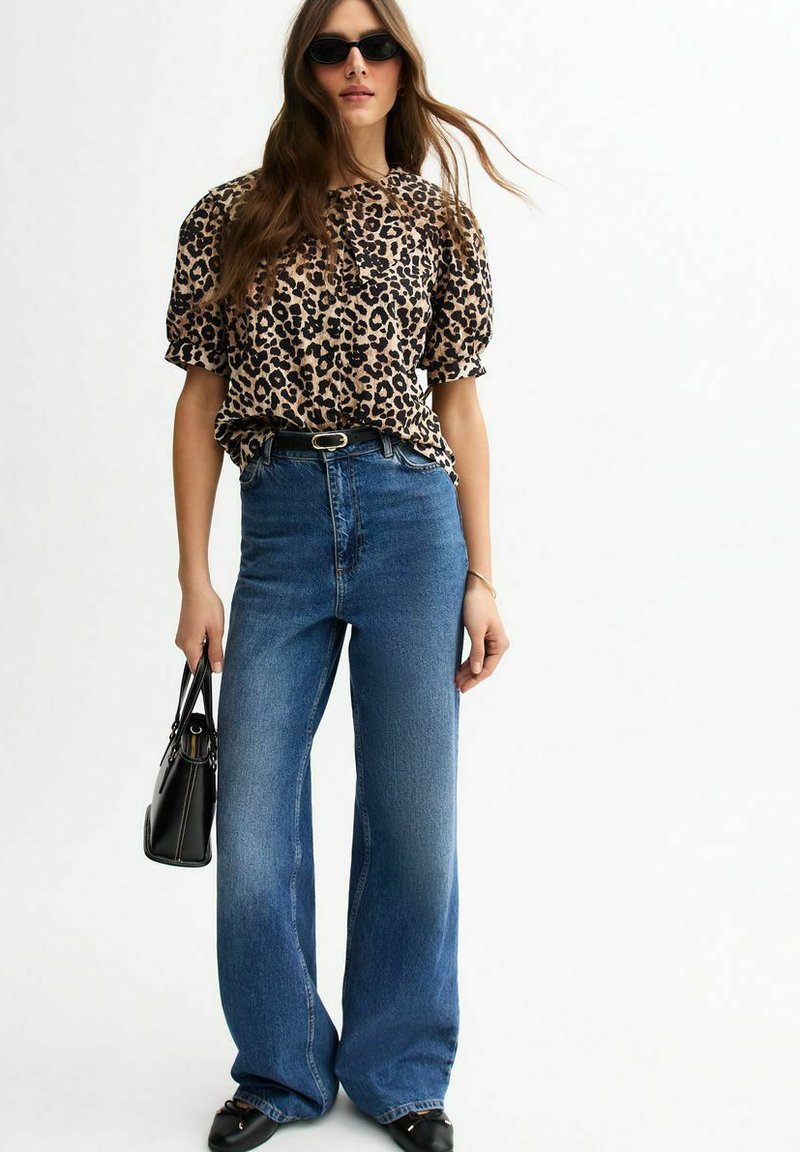 Blouse met luipaardprint en korte mouwen, hoge taille met wijde blauwe jeans en zwarte handtas. Glad materiaal en een losse fit. Zwarte zonnebril.