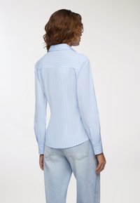 Camicia a righe azzurre con colletto a punta, maniche lunghe e polsini abbottonati. Vestibilità sartoriale con orlo arrotondato e yoke posteriore.