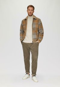 Braun kariertes Jackett mit grauen Akzenten, cremefarbener Rollkragenpullover, olivfarbene Cordhosen und weiße Sneakers mit schwarzen Details, alles passgenau und lässig.