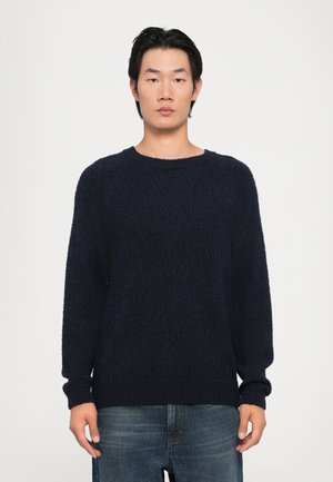 Marineblauer gestrickter Pullover mit lockerer Passform, rundem Ausschnitt und gerippten Bündchen und Saum. Die Textur wirkt weich und flauschig.