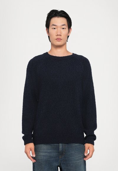 Pull en tricot bleu marine avec une coupe décontractée, un col rond et des poignets et un ourlet côtelés. La texture semble douce et duveteuse.