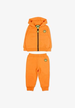 Ensemble pour tout-petit composé d'un sweat à capuche et d'un pantalon orange avec une fermeture éclair noire, des écussons jaunes représentant un visage souriant avec une empreinte de patte sur la poitrine, la tirette de la fermeture éclair et le pantalon.