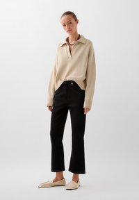 Beige knitted pullover with a collar, paired with black flared jeans featuring a colorful accent on the waistband, and light shoes.