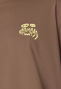 Brown t-shirt made of soft fabric featuring a yellow abstract graphic and text design on the left chest area.