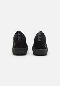 Zapatillas deportivas negras con parte superior de ante y malla. Presentan una suela de goma texturizada y un distintivo tirador triangular en el talón.