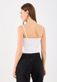 Witte getailleerde tanktop met dunne spaghettibandjes, gecombineerd met hoge zwarte jeans met achterzakken en een gladde textuur.