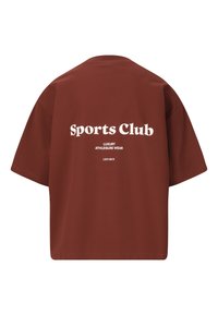 Rostfärgad kortärmad t-shirt med vit text som säger "Sports Club" och "Luxury Athleisure Wear" på baksidan. Slät bomullstyg.