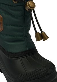 Botte isolante verte avec un design matelassé, une section inférieure en caoutchouc et une semelle texturée noire. Dotée de ferrures en bronze et d'une fermeture à cordon de serrage.