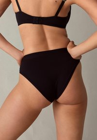 Culotte nera in cotone a vita alta con texture liscia e design senza cuciture, dotate di una gamba bassa e di una morbida fascia in vita.