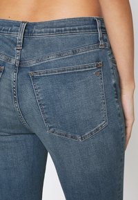 Mörkblå denimjeans med medelhög midja, fem fickor och en slät yta. Har subtila sömmar och en klassisk design.