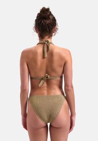 Złoty bikini błyszczące z dekoltem halter. Posiada wiązania na szyi i plecach oraz niskie figi o minimalnym pokryciu.